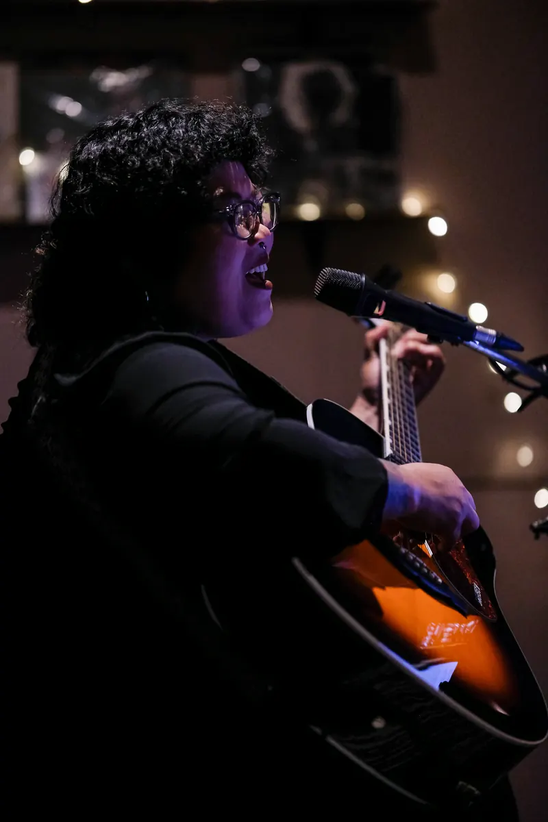 Live music — a singer with a guitar under the string lights · Vermut Café, רחוב ההליכה בפאי
