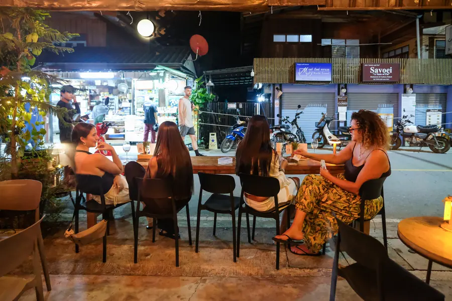 A table by the walking street at night, the street going by · Vermut Café, רחוב ההליכה בפאי