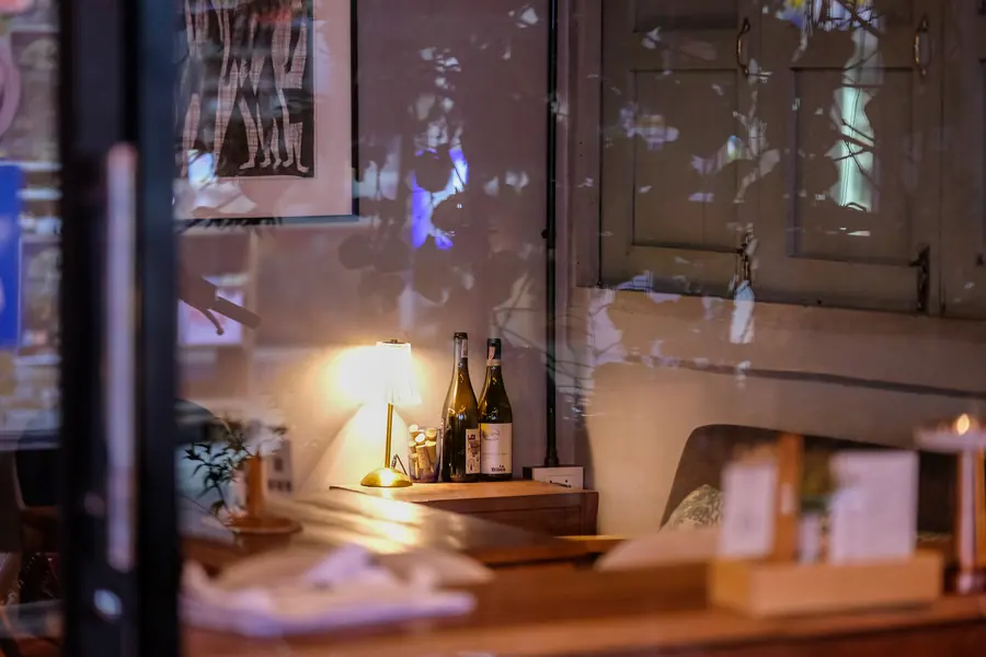 A table lamp and two bottles by the window, the street reflected in the glass · Vermut Café, Pai Walking Street