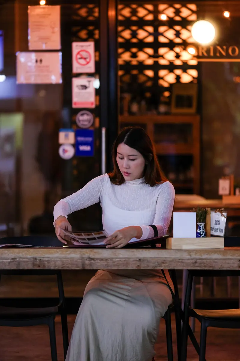 A guest reading the menu on her own at a ground-floor table · Vermut Café, רחוב ההליכה בפאי