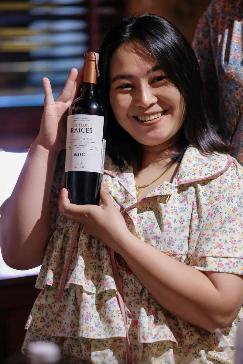 A guest holding a bottle of red, smiling · Vermut Café, Pai Walking Street