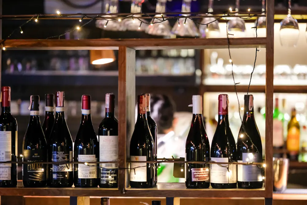 Rows of red wine on the back shelf, glasses hanging above · Vermut Café, רחוב ההליכה בפאי