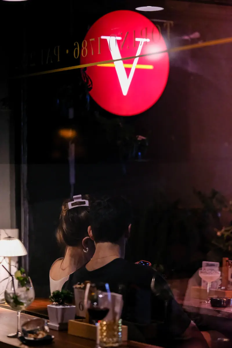 The red V seen through the terrace window, a guest at the table · Vermut Café, Pai Walking Street