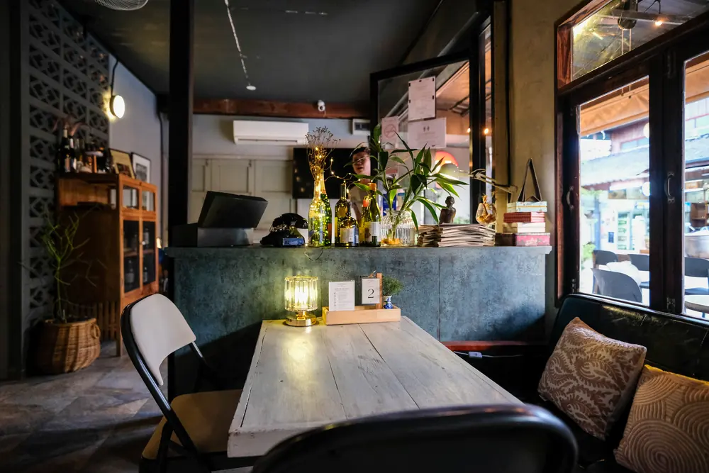 A long table with a lamp, cushions on the bench, ground floor · Vermut Café, Pai Walking Street