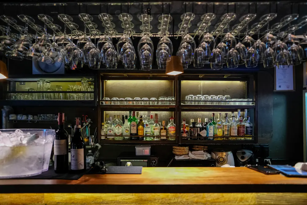 The counter with the back bar lit and glasses hanging above · Vermut Café, רחוב ההליכה בפאי