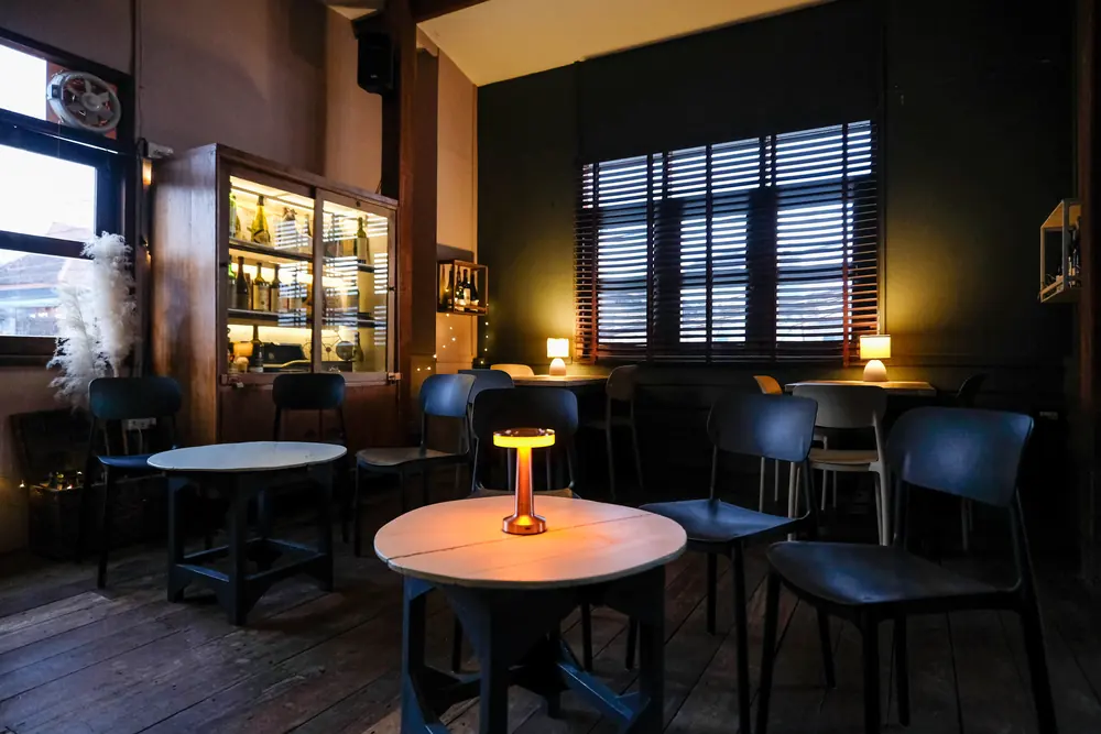 A round table with a lamp by the shutters, chairs around it · Vermut Café, Pai Walking Street