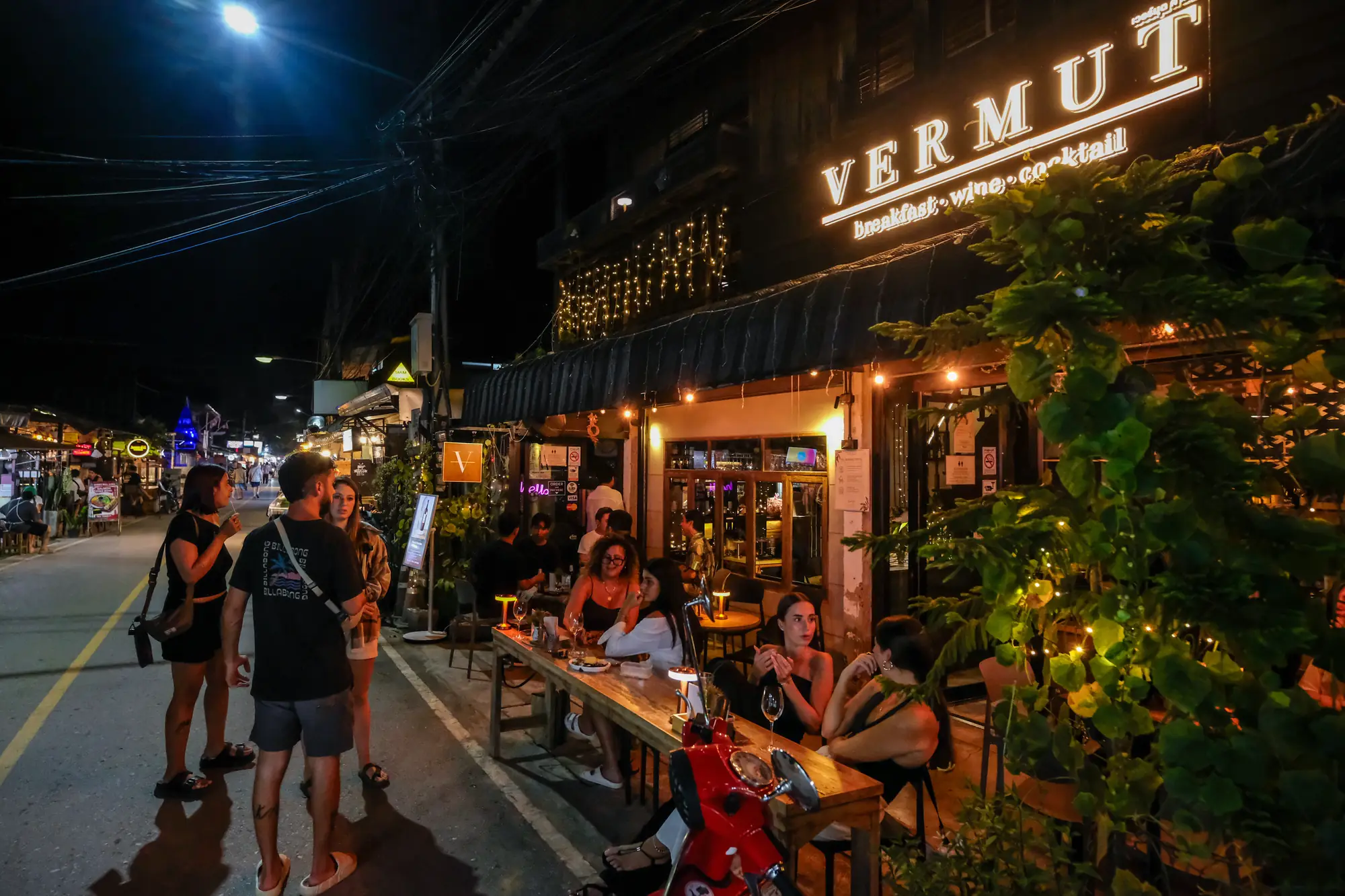 Pai Walking Street at night — Vermut café lit on the right, guests at the front tables, the street filling up · Vermut Café, Pai Walking Street