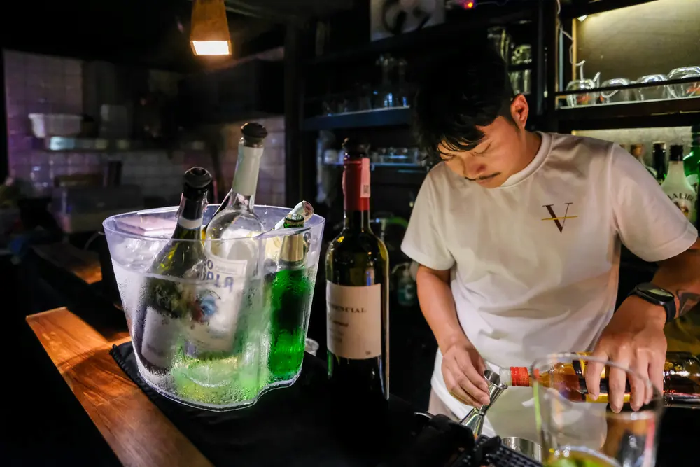 Bottles on ice beside the bartender measuring a pour · Vermut Café, Pai Walking Street